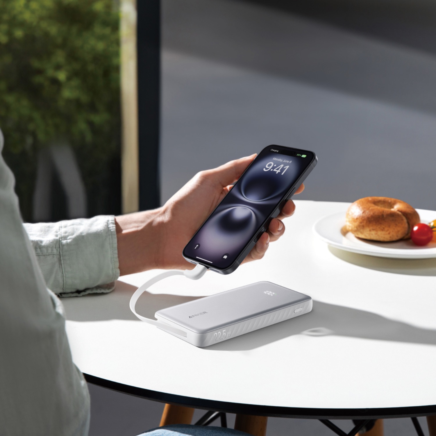 White Anker Zolo 10000mAh 22.5W power bank charging a smartphone on a tabletop with the built-in USB-C cable.